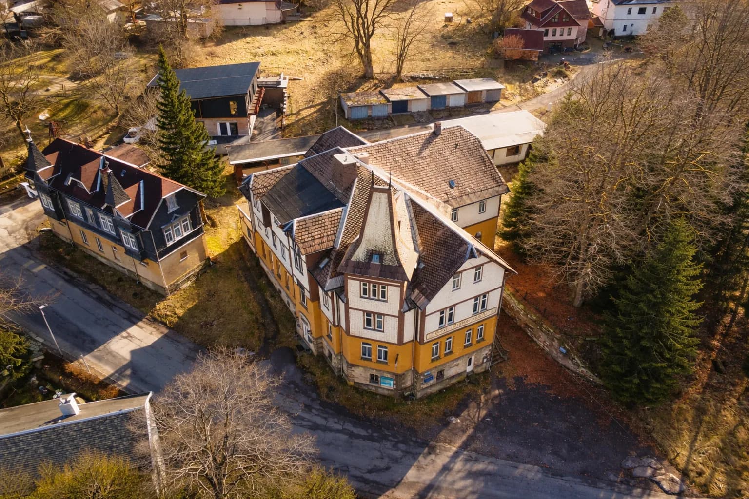 Drohnenaufnahme des Hotelensembles „Schwarzaquelle“ aus der Vogelperspektive im Abendlicht mit komplexer Dachlandschaft, Turmaufbau, Nebengebäuden, Garagenzeile und Waldrandlage.
