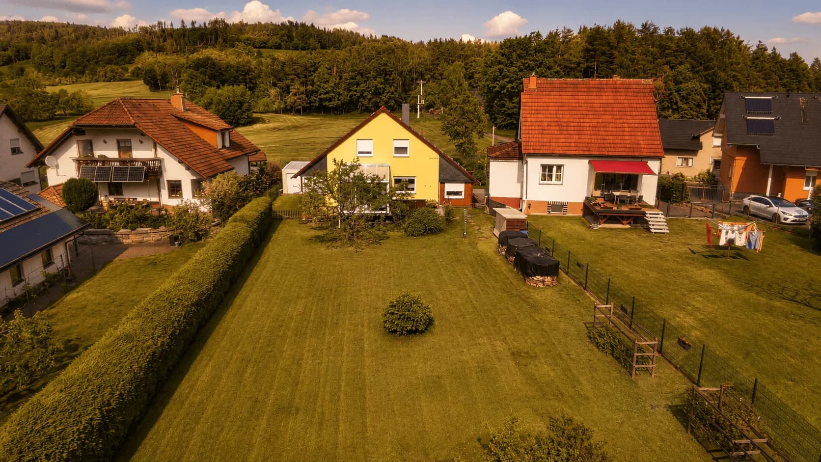 Luftbild des weitläufigen Rückgartens mit gepflegter Rasenfläche, grüner Hecke und Waldrand im Hintergrund.