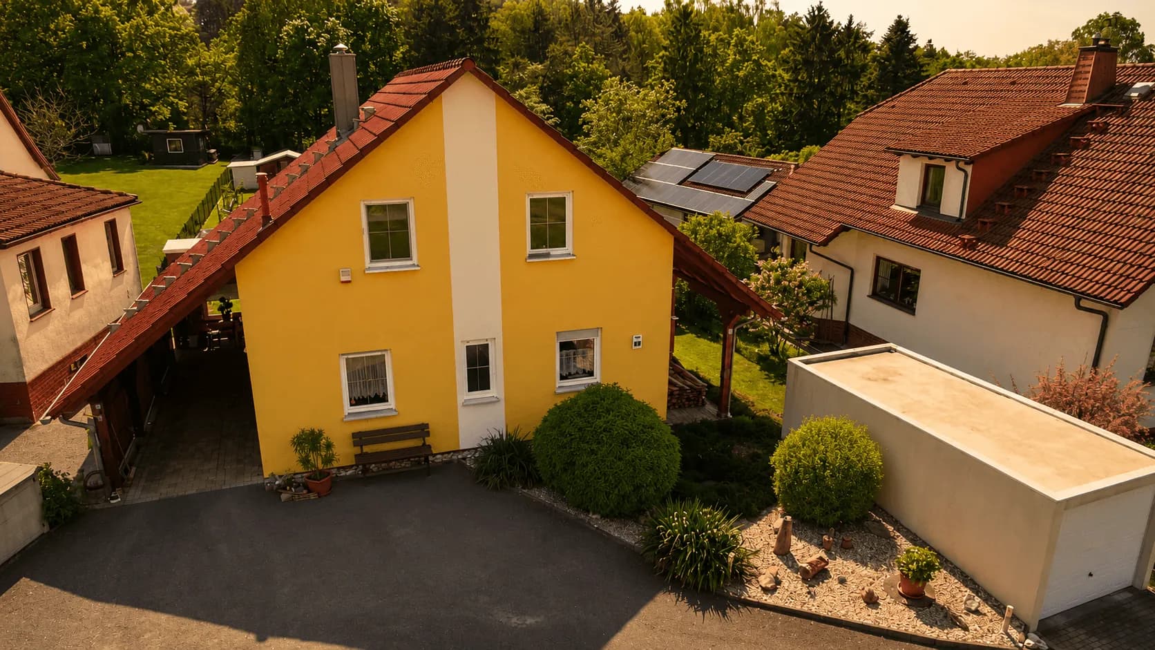Vorderansicht des gepflegten gelben Einfamilienhauses mit Hofeinfahrt, Carport und separater Garage.