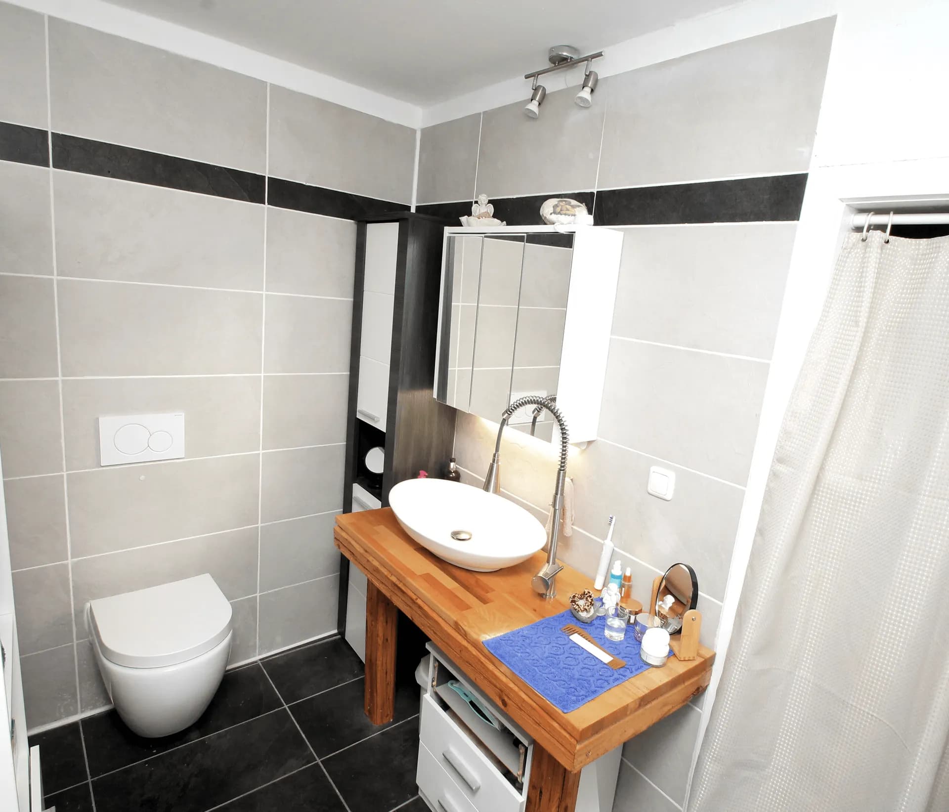Stilvolles Badezimmer mit hellen Wandfliesen, Hänge-WC, Spiegelschrank sowie rustikalem Holzwaschtisch mit modernem Aufsatzwaschbecken.