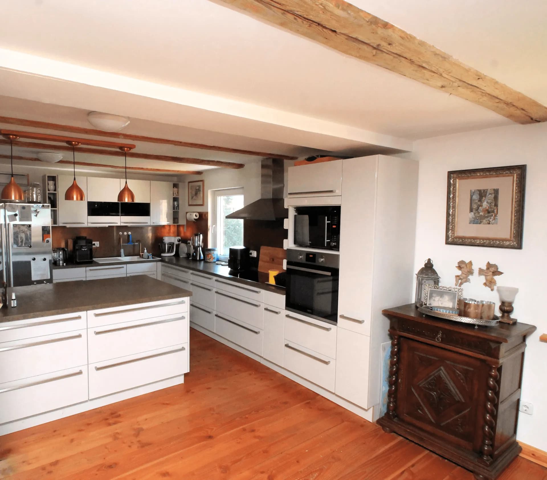 Großzügige moderne Landhausküche mit massiven Deckenbalken, Kücheninsel, hochwertigen Einbaugeräten und echtem Holzdielenboden.
