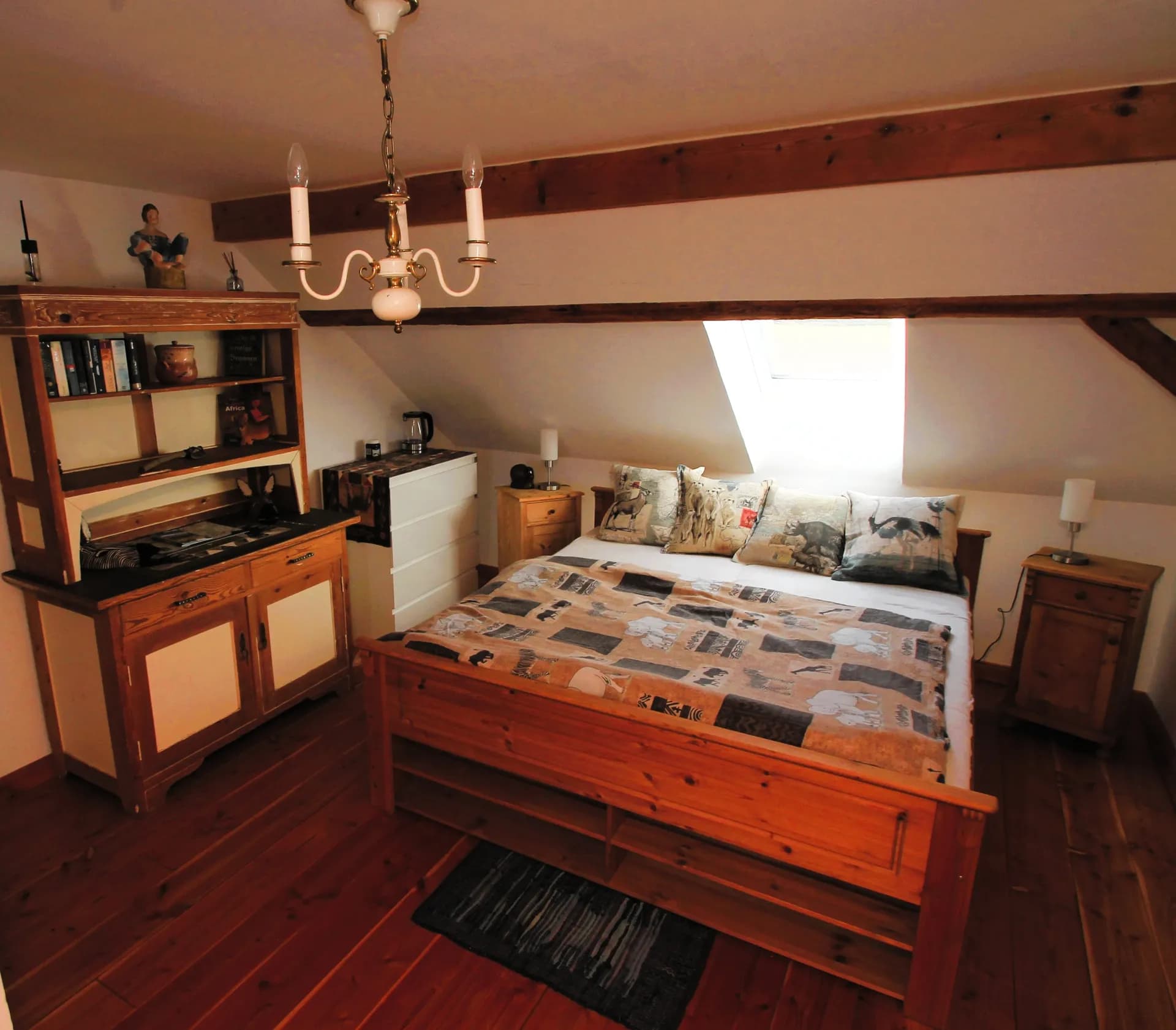 Gemütliches Schlafzimmer im Dachgeschoss mit Doppelbett aus Massivholz, Nachttischen, Dachfenster, sichtbarer Balkenlage und rustikalem Bauernschrank.