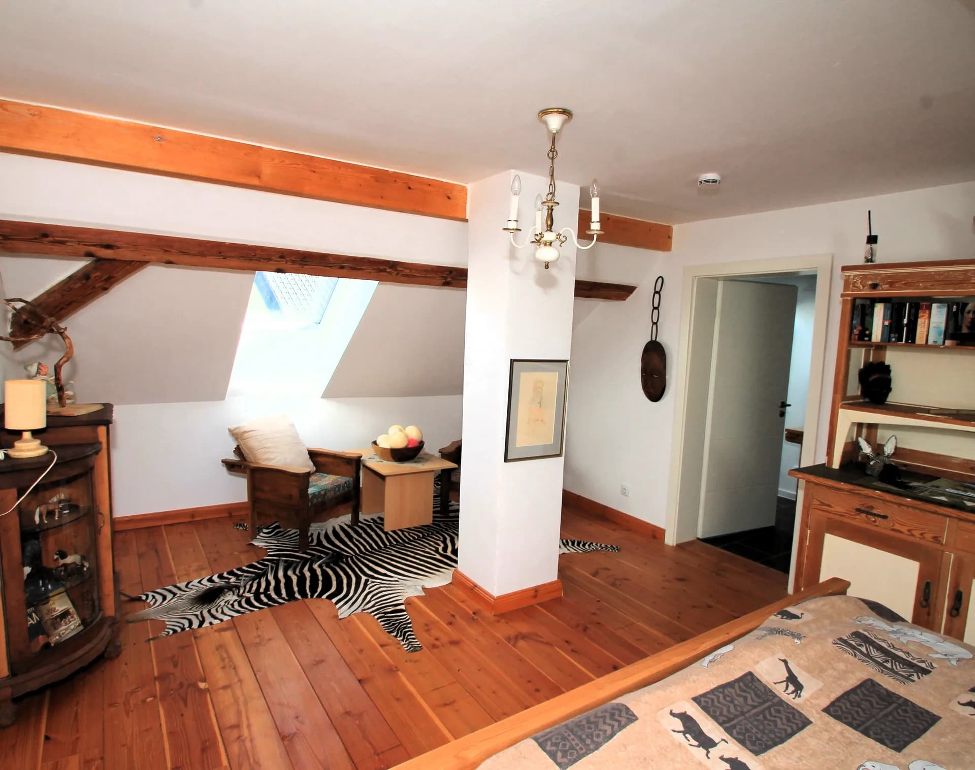 Gemütliches Dachgeschoss-Schlafzimmer mit sichtbaren Holzbalken, Dachflächenfenster, integrierter Sitzecke, gepflegtem Holzdielenboden und stilvollem rustikalem Mobiliar.