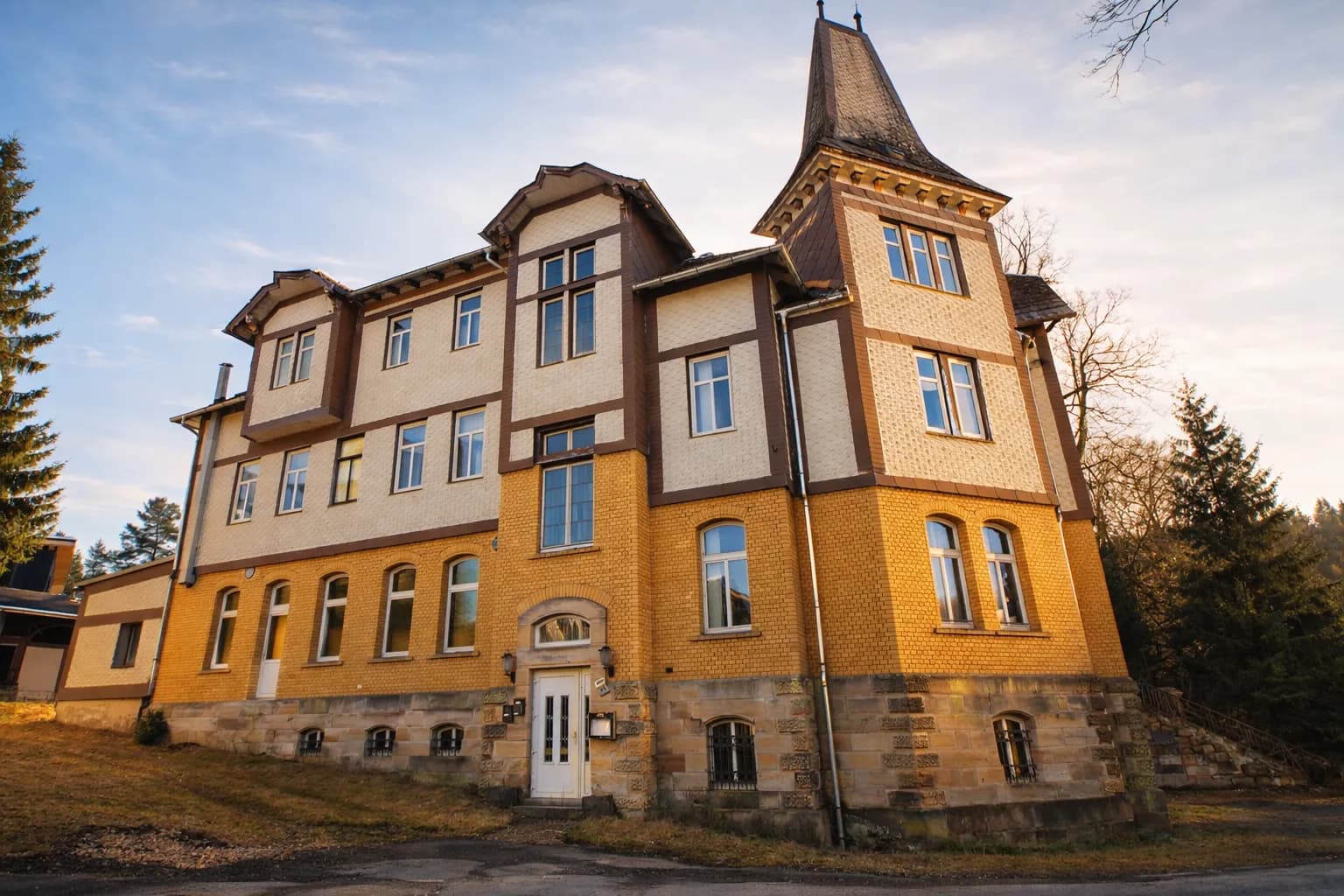 Perspektivische Fassadenansicht des Hotels „Schwarzaquelle“ mit Bogenfenstern, Ziergiebeln, repräsentativem Eingangsportal und rustikalem Sandsteinsockel mit vergitterten Kellerfenstern.