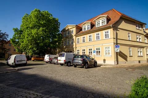 Eckansicht der historischen Hotel- und Gewerbeimmobilie „Goldene Henne“ mit Dreiecksgiebeln, Dachgauben, Ziegeldach und gepflastertem Parkplatzbereich.