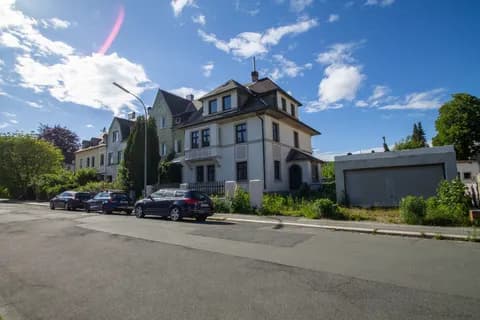 Straßenansicht und Umgebung des Mehrfamilienhauses mit Nebengebäude/Garage, Vorgarten und Parkmöglichkeiten am Straßenrand.